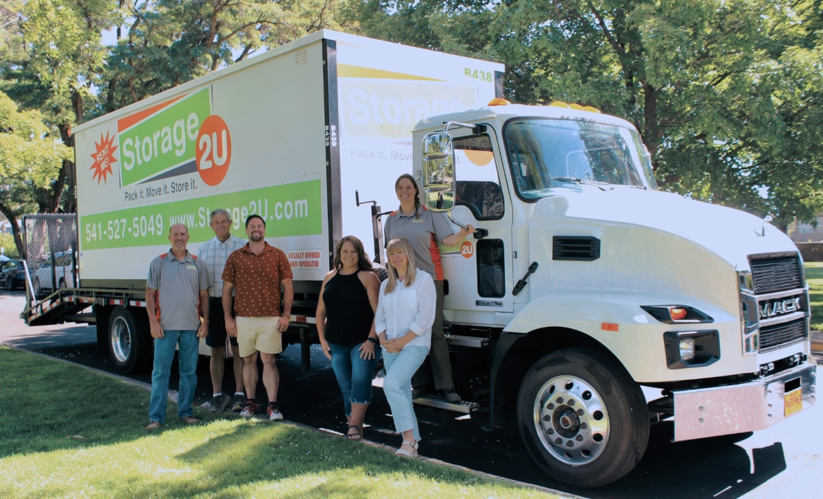 A group of people standing in front of a Storage 2U moving truck on the street